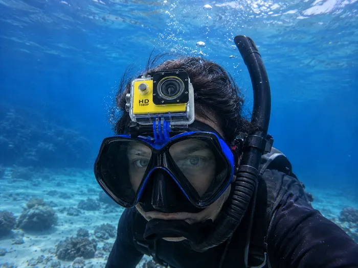 Scuba diver wearing a diving mask with a yellow action camera mounted on top in clear blue ocean water